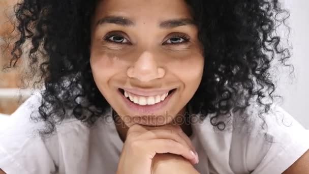 Афро-американка лежит на животе в постели улыбаясь, смотря в камеру, смеясь — стоковое видео