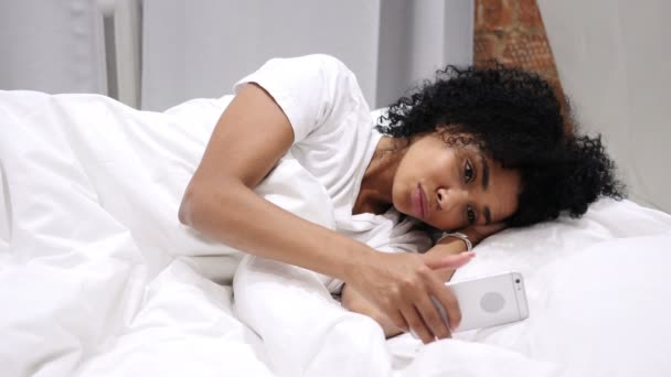 Afroamerikanerin surft auf Smartphone, E-Mail und Nachrichten und liegt nebeneinander im Bett — Stockvideo