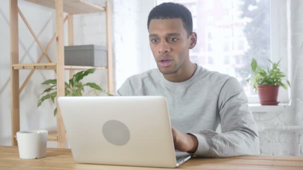 Захоплений афроамериканський чоловік святкує успіх під час роботи на ноутбуці, сидячи на дивані — стокове відео