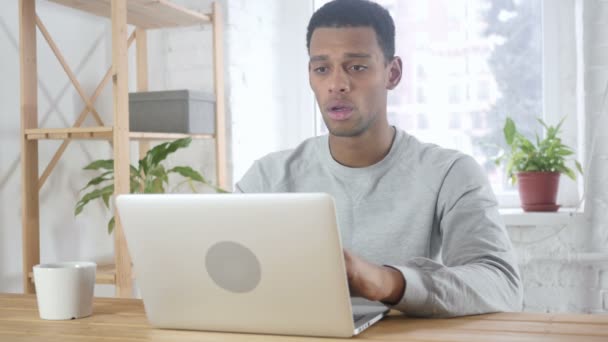 Homem afro-americano sentado no escritório perturbado por perda, trabalhando no laptop — Vídeo de Stock