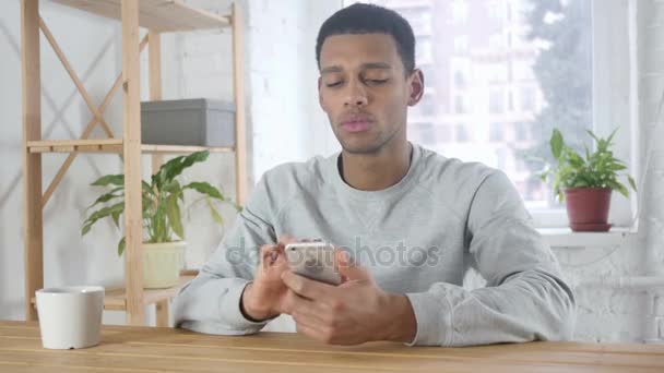 Hombre africano navegando en línea en el teléfono inteligente, escribiendo mensaje — Vídeo de stock