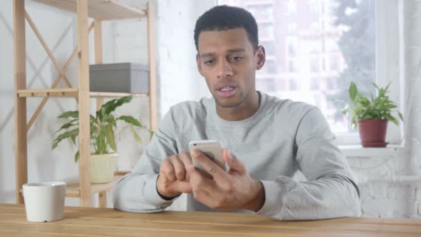 Afro-amerykański człowiek zdenerwowany przez straty, szukam wyników na smartfonie — Wideo stockowe