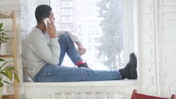 Afro-Amerikan oturma pencere ve cep telefonu üzerinde konuşurken adam — Stok video