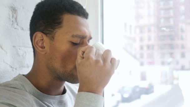 Крупним планом афроамериканський чоловік п'є каву, дивлячись крізь вікно — стокове відео