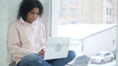 Laptop, pencereden bakarak çalışan genç Afro-Amerikan kadın