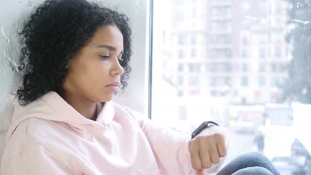Afro-American žena čekání a sledování času, sedí u okna — Stock video