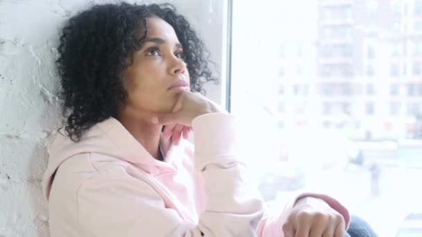 Νεαρή αφρικανική γυναίκα σκέφτεται και την ανταλλαγή απόψεων, κάθεται στο παράθυρο — Αρχείο Βίντεο