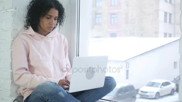 Afroamerikansk kvinde arbejder på bærbar computer, sidder ved vinduet – Stock-video