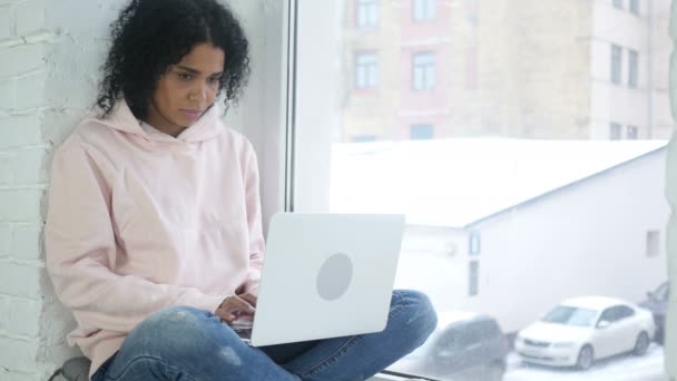 Jovem mulher afro-americana trabalhando no laptop, olhando através da janela — Vídeo de Stock