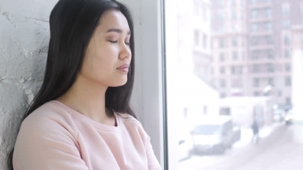 Возбужденная молодая азиатка, жгущая пальчики вверх, сидящая у окна — стоковое видео