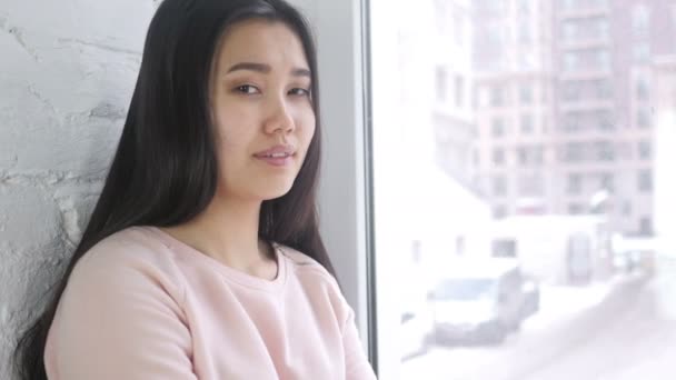 Fiatal ázsiai nő integetett kézzel szívesen, ül az ablakban — Stock videók