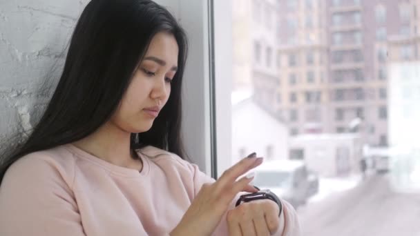 젊은 아시아 여성 Smartwatch 사용 하 여 탐색, 창이에 앉아 — 비디오