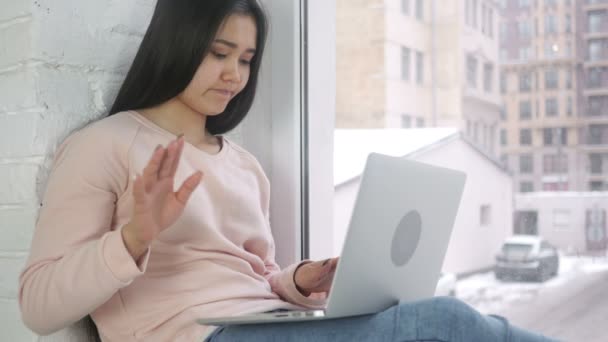 Молодая азиатка в отчаянии и гневе работает над ноутбуком, сидит у окна — стоковое видео