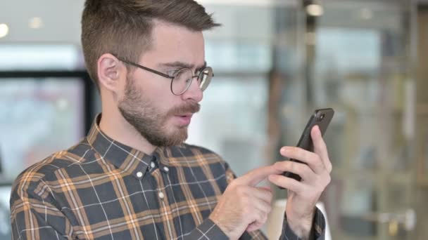 Porträt eines traurigen jungen Designers, der sein Smartphone verliert — Stockvideo