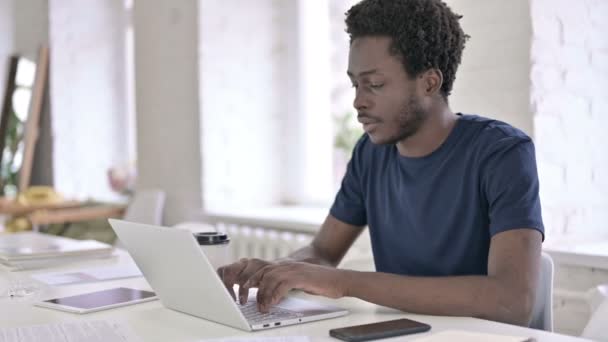 Jonge Afrikaanse man drinken koffie en werken op laptop — Stockvideo
