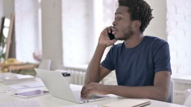 Ofiste akıllı telefondan konuşan genç Afrikalı adam.
