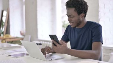 Akıllı telefon kullanan ve dizüstü bilgisayarda çalışan odaklanmış Afrikalı Adam