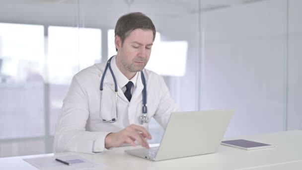 Médico de mediana edad enfocado que trabaja en el ordenador portátil — Vídeos de Stock