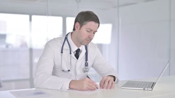 Ernstige middelbare leeftijd Doctor doet papierwerk in Office — Stockvideo