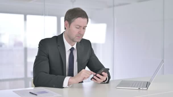 Alegre hombre de negocios de mediana edad utilizando Smartphone en la oficina — Vídeo de stock