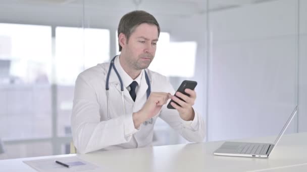 Atractivo médico de mediana edad usando Smartphone en la oficina — Vídeos de Stock