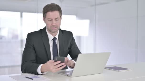 Fokuserad affärsman som använder smartphone och arbetar på laptop — Stockvideo