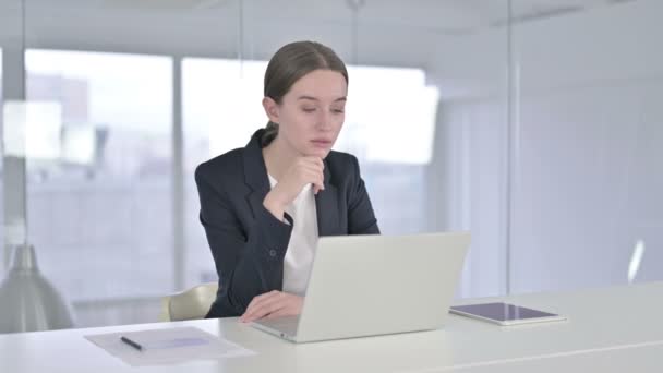 Joven empresaria pensando y trabajando en el ordenador portátil en la oficina — Vídeo de stock