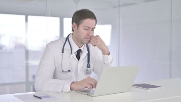 Médico de mediana edad que piensa y trabaja en el ordenador portátil — Vídeo de stock