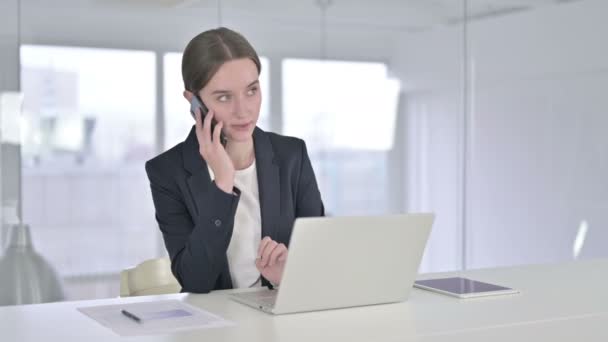 Glückliche junge Geschäftsfrau, die im Büro per Smartphone spricht — Stockvideo