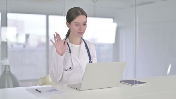 Весела молода жінка-лікар робить відеочат на ноутбуці — стокове відео