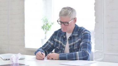 Hayal kırıklığına uğramış orta yaşlı bir adam kağıda yazmaya çalışıyor. 