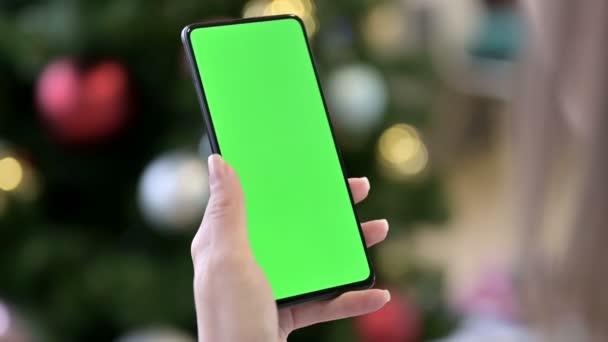Жіноча рука тримає Chroma Key Screen смартфон біля різдвяної ялинки — стокове відео