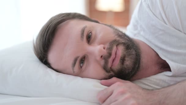Detailní záběr veselého vousu Mladý muž s úsměvem na kameru v posteli — Stock video