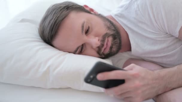 Close-up van de baard jonge man met behulp van smartphone in bed — Stockvideo