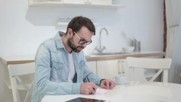 Homem jovem barba Pensando e escrevendo em papel no escritório — Vídeo de Stock