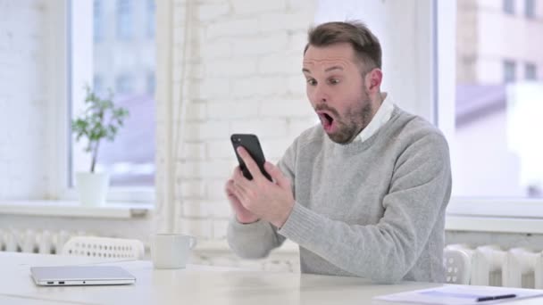 Emocionado hombre celebrando el éxito en el teléfono inteligente en el trabajo — Vídeos de Stock