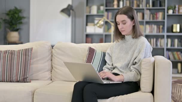 Φιλόδοξη νεαρή γυναίκα που εργάζεται σε φορητό υπολογιστή στον καναπέ — Αρχείο Βίντεο