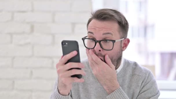 スマートフォンで損失に反応する衝撃的な創造的な男 — ストック動画