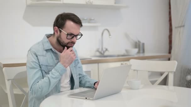 Serieuze jonge baard jonge man denken en werken op laptop — Stockvideo