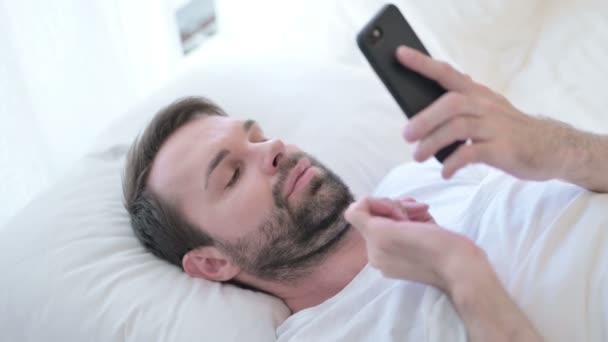 Designer jovem barba atraente usando Smartphone na cama — Vídeo de Stock