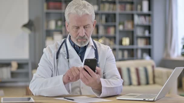 Fokuserad äldre läkare använder smartphone på kliniken — Stockvideo