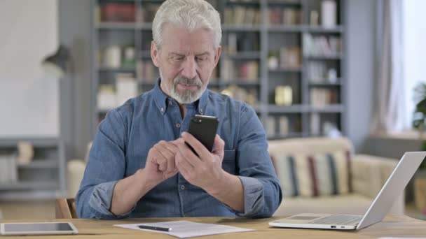 Fokuserad äldre gubbe som använder smartphone i det moderna kontoret — Stockvideo