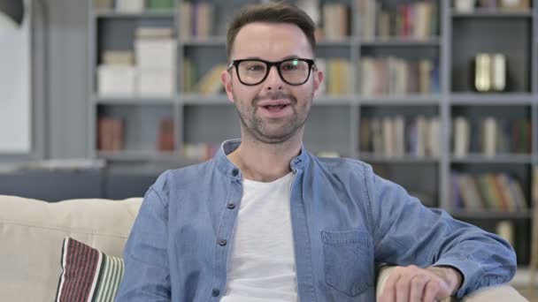 Porträt eines fröhlichen jungen Mannes, der auf dem Sofa sitzt und lächelt — Stockvideo