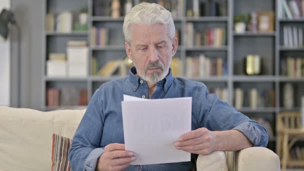 Porträt eines älteren Mannes beim Lesen von Dokumenten auf dem Sofa — Stockvideo