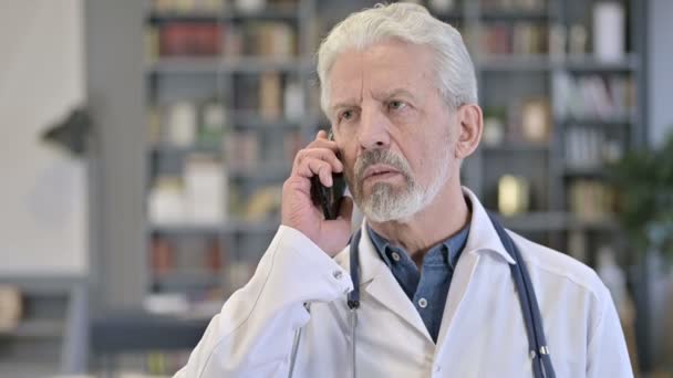 Porträt eines fokussierten alten Arztes, der mit dem Smartphone spricht