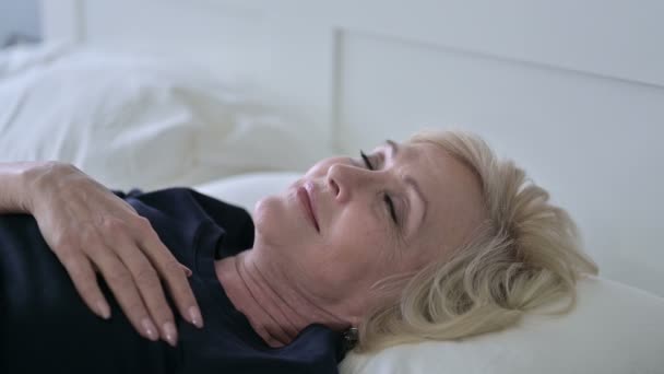Nachdenkliche alte Frau wacht im Bett auf — Stockvideo