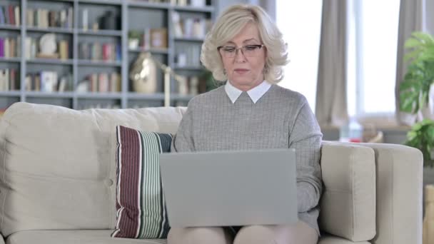 Serious Old Woman Sentado en el sofá y utilizando el ordenador portátil — Vídeo de stock