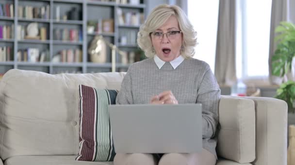 Gammal kvinna sitter på soffan och reagerar på misslyckande på laptop — Stockvideo