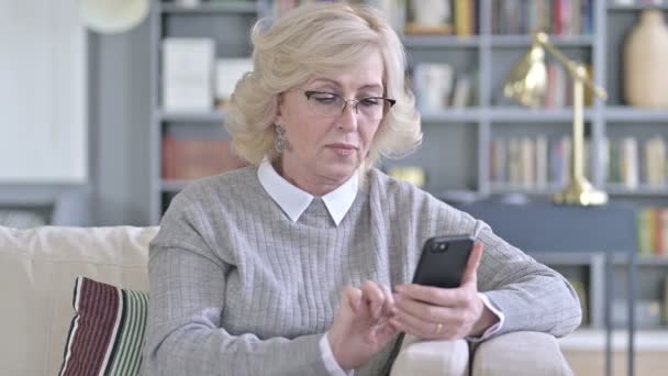 Vieille femme célèbre le succès sur Smartphone sur canapé — Video