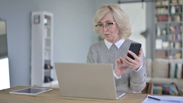 Mulher velha usando telefone inteligente e trabalhando no laptop — Vídeo de Stock